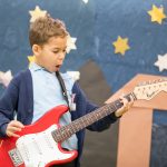 Image of Alessandro in Year 3 playing an electric guitar in front of a set of an Early years production.