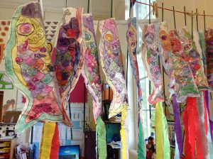 A washing line is full of painted paper fish with ribbons streaming from the bottom of each one to represent Japanese Koinobori.