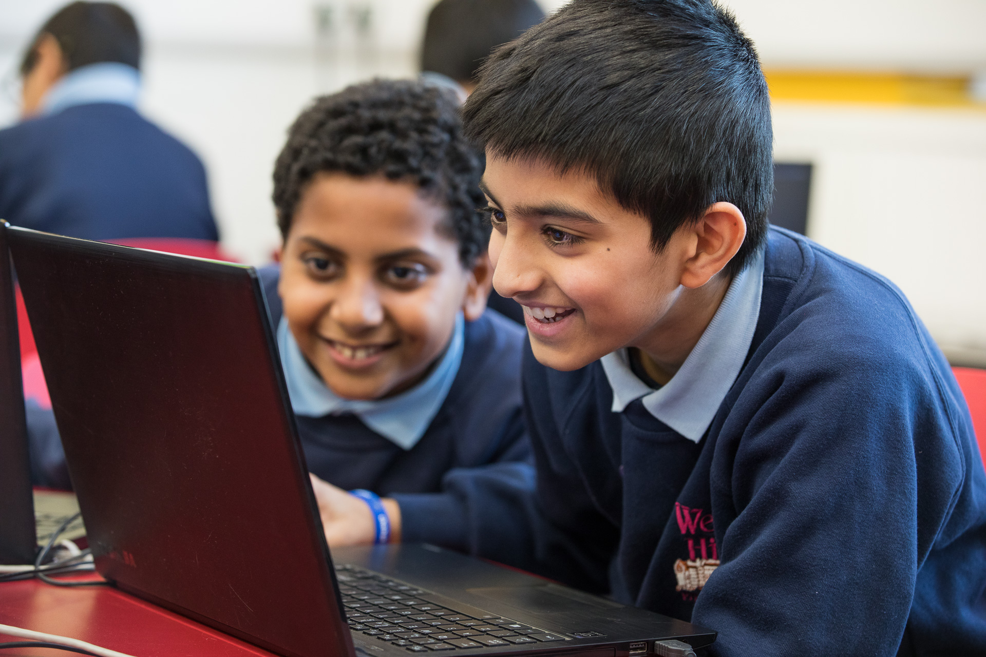 Image of two boys are looking at a lap top in the computing suite