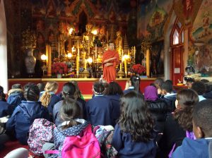 Image of Year 5 in a Buddhist temple listening to a monk telling them about his religion.