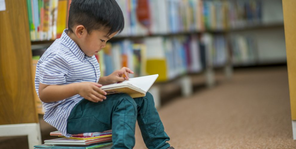 image of a small boy sitting on a pile of books in a library reading a book