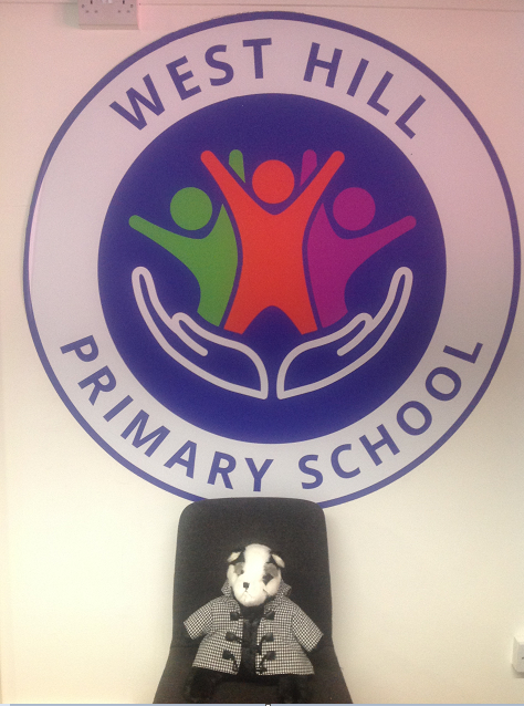 Image of Belle the Badger soft toy in front of school logo